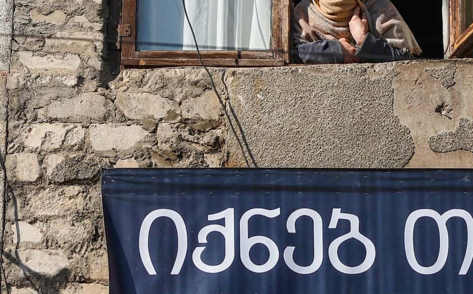 Diana Davlianidze, 49, looks out from the window by the banner, “Maybe at least you can be helped.” On January 16, Zurab Kiria, 52, an IDP, killed himself. According to his neighbours, his last words were, “Maybe at least you can be helped.” Diana Davlianidze, 49, looks out from the window by the banner, “Maybe at least you can be helped.” On January 16, Zurab Kiria, 52, an IDP, killed himself. According to his neighbours, his last words were, “Maybe at least you can be helped.”